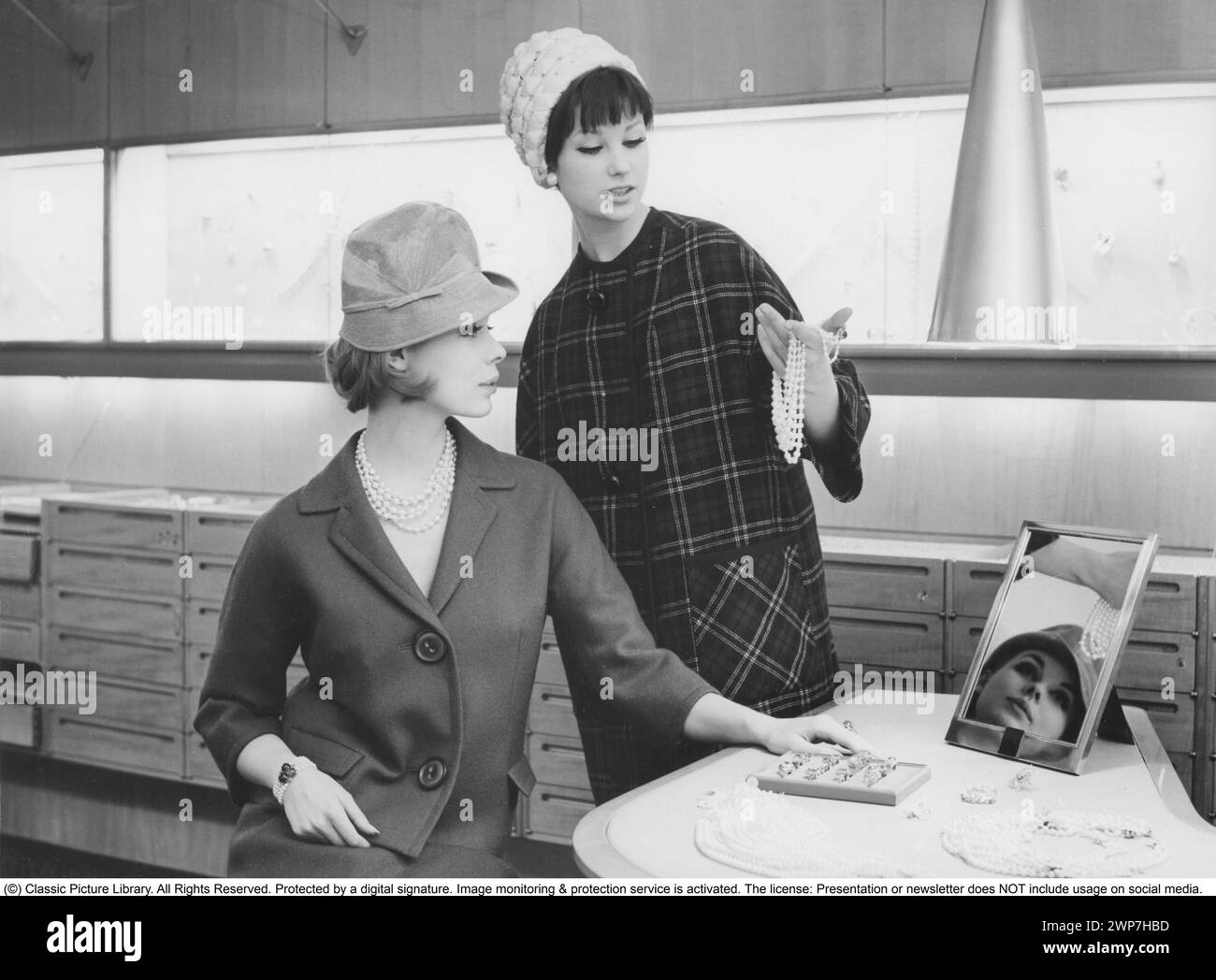 Dans les années 1960 Deux femmes dans des vêtements typiques des années 1960, maquillage et coiffure dans une bijouterie, regardant un collier de perles. Banque D'Images