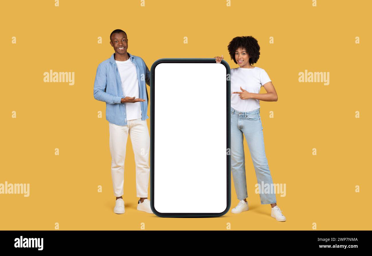 Couple afro-américain engageant présentant un grand écran de smartphone blanc vertical Banque D'Images