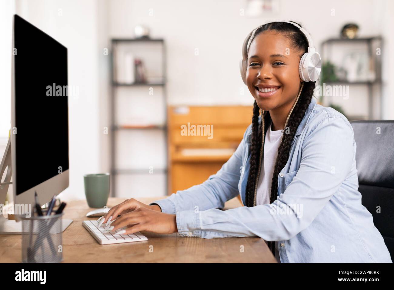 Heureuse étudiante noire dans des écouteurs se livrant à des études en ligne Banque D'Images