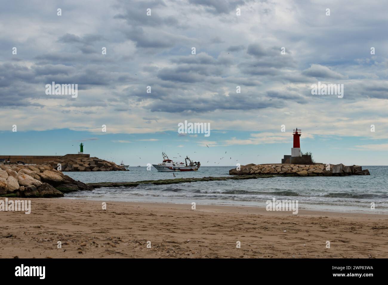 Villajoyosa, Espagne, 04 mars 2024:paysage maritime avec bateau de pêche entrant dans le port de Villajoyosa à côté du phare et ciel nuageux au Banque D'Images