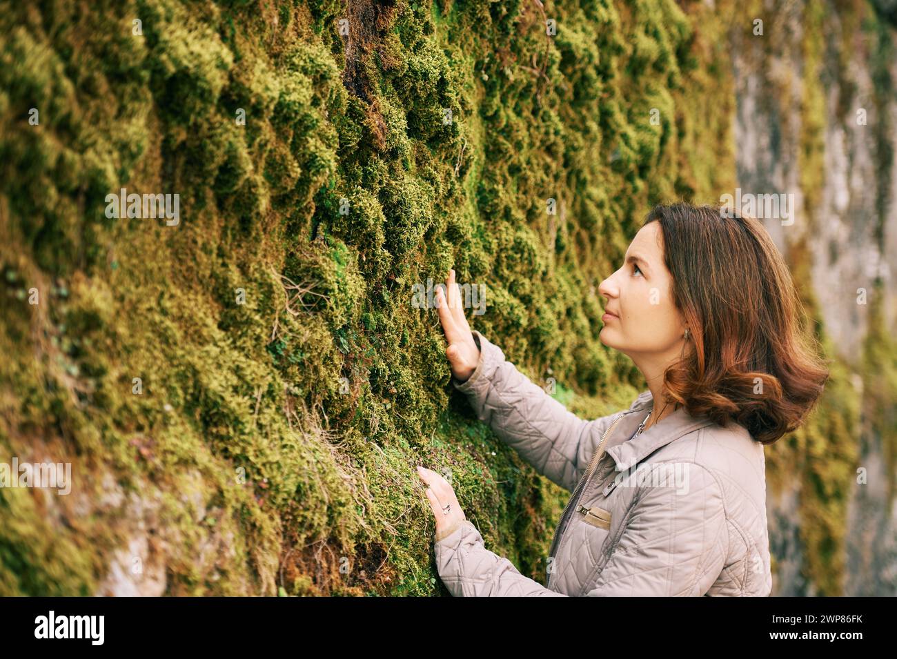 Portrait extérieur de belle femme heureuse profitant d'une belle journée à l'extérieur, posant avec mur de mousse Banque D'Images