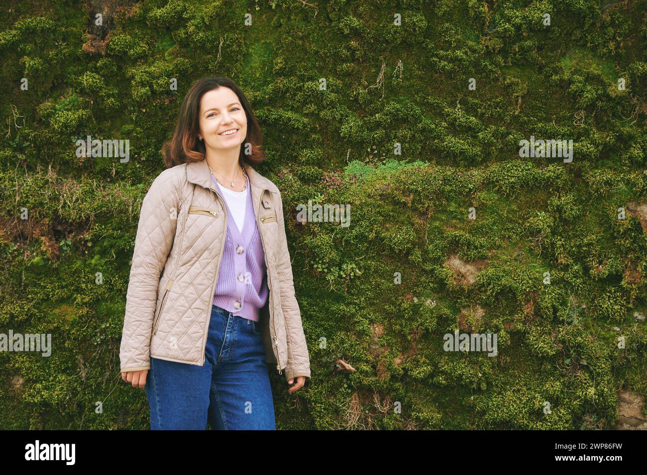 Portrait extérieur de belle femme heureuse profitant d'une belle journée à l'extérieur, posant avec mur de mousse Banque D'Images