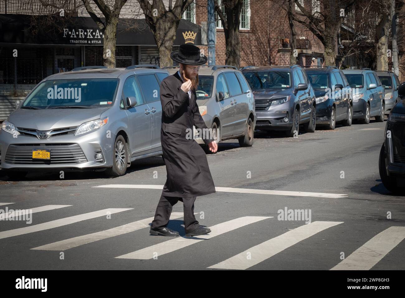 Un homme juif orthodoxe boucle son peyus en traversant une rue à Brooklyn, New York. Banque D'Images