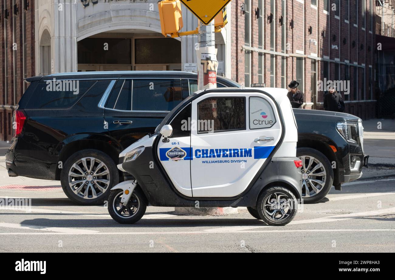 GROS PETIT. Une grosse Cadillac Denali garée derrière un minuscule mini-véhicule Chaverim à 3 roues à Williamsburg, Brooklyn, New York. Banque D'Images