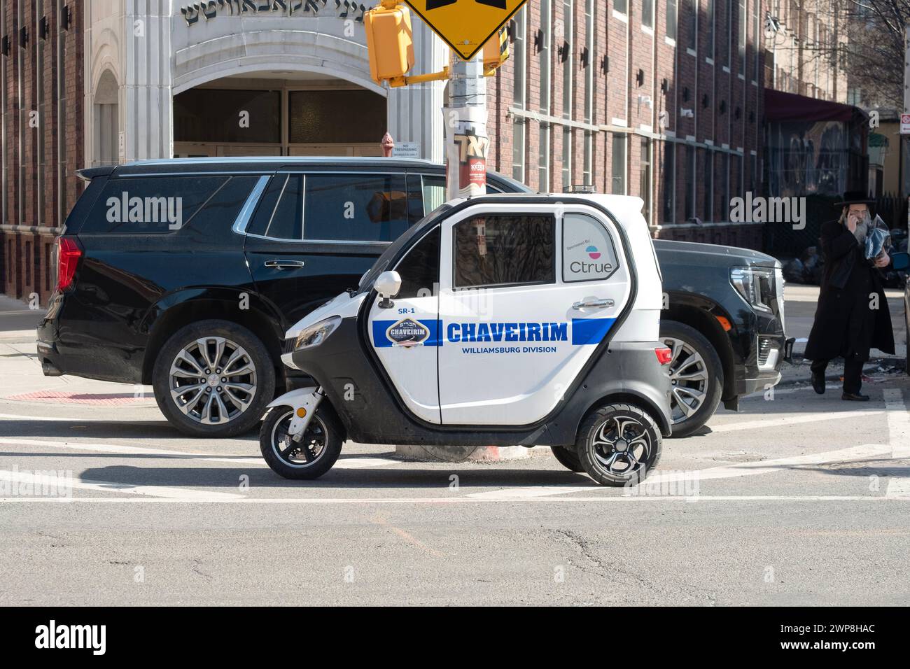 ÉNORME MINUSCULE. Une grosse Cadillac Denali garée derrière un minuscule mini-véhicule Chaverim à 3 roues à Williamsburg, Brooklyn, New York. Banque D'Images