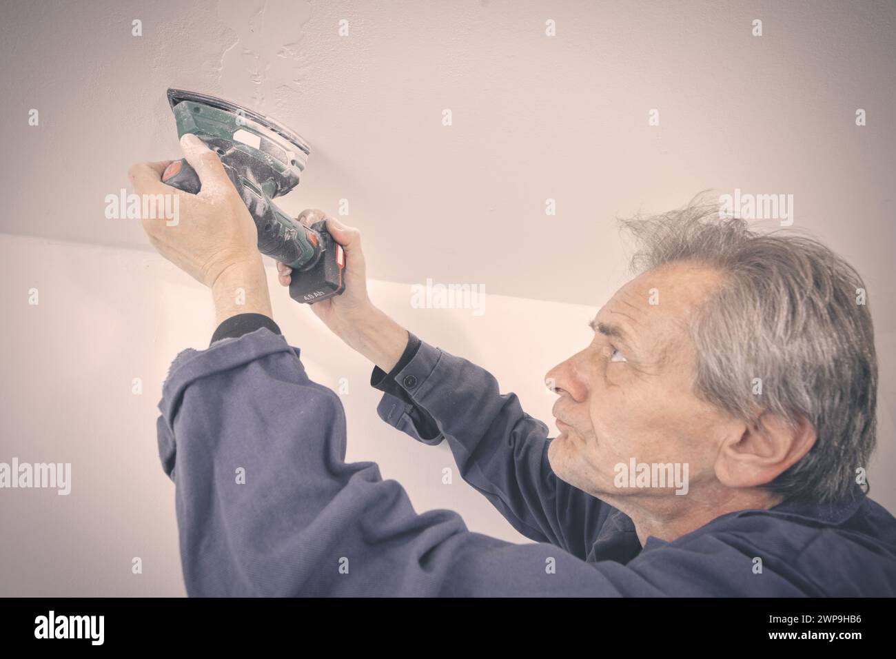 Homme plus âgé réparant et ponçant le plafond dans l'appartement vide Banque D'Images