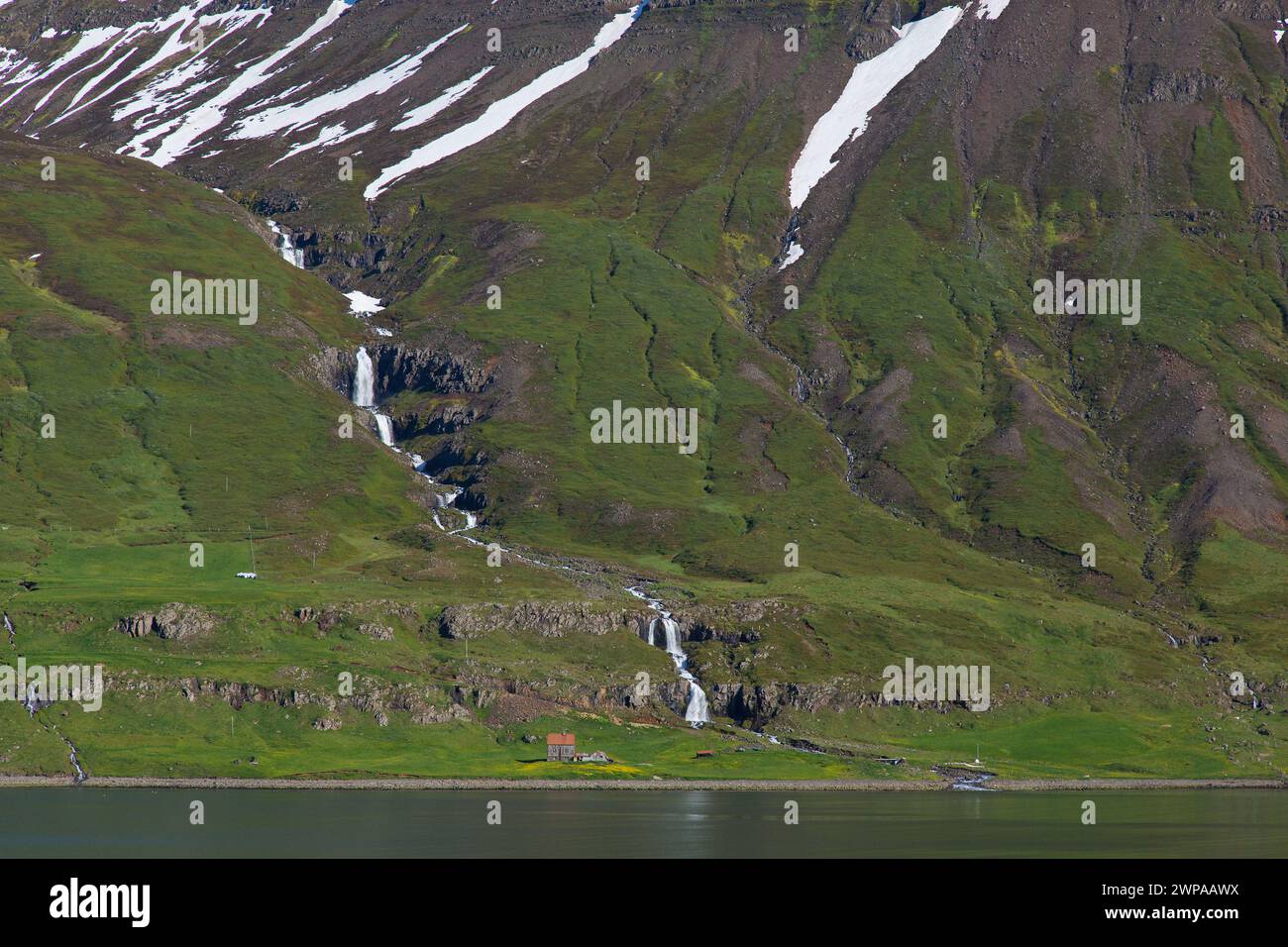 Cascade et ferme désolée le long du fjord Seyðisfjörður / Seydisfjoerdur en été, région orientale / Austurland, Islande Banque D'Images