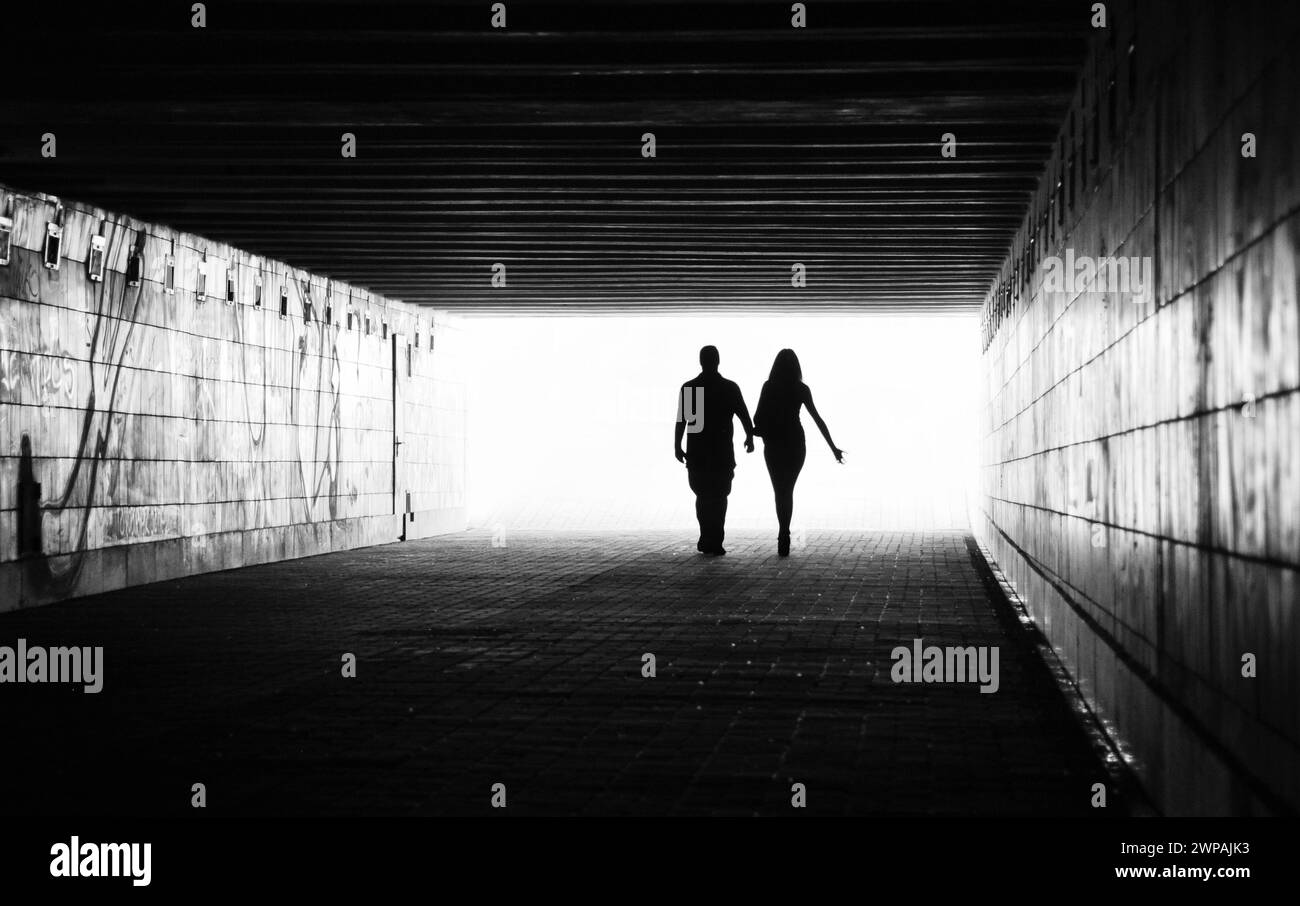 Silhouettes de deux personnes dans un tunnel - figures masculines et féminines. Image en noir et blanc avec lumière venant de derrière. Couple s'éloignant. Banque D'Images