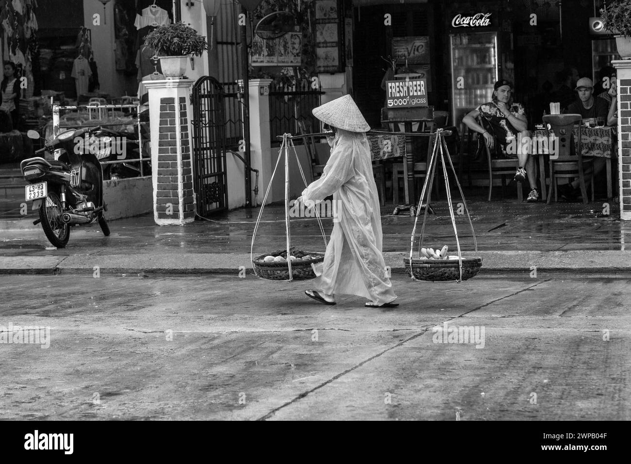 Hoi an, Vietnam ; scène de rue de la vieille ville. Jeune femme portant sa marchandise sur un poteau en bambou d'épaule Banque D'Images