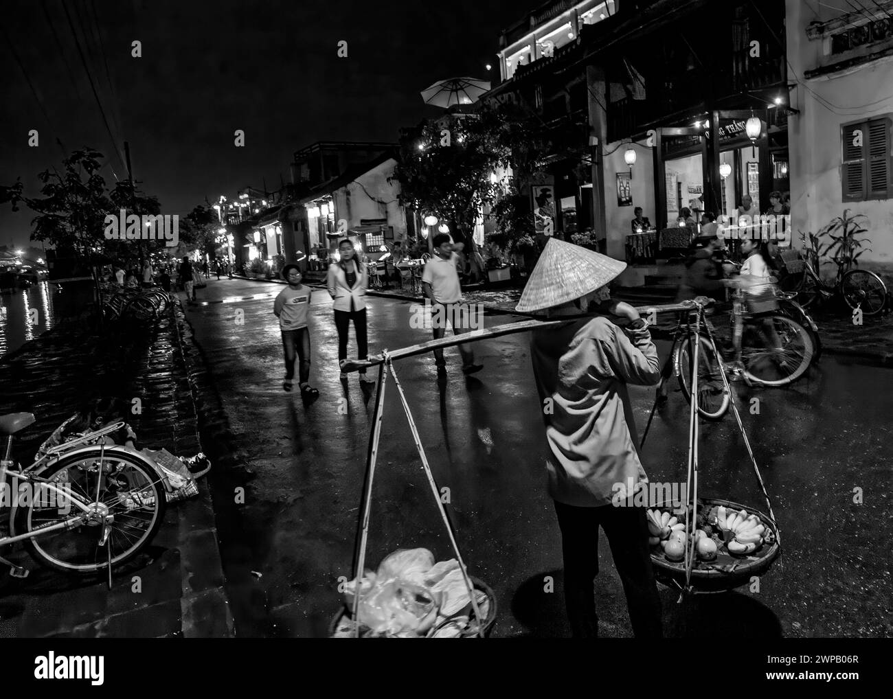 Hoi an, Vietnam ; scène de rue nocturne de la vieille ville. Jeune femme portant sa marchandise sur un poteau en bambou d'épaule Banque D'Images