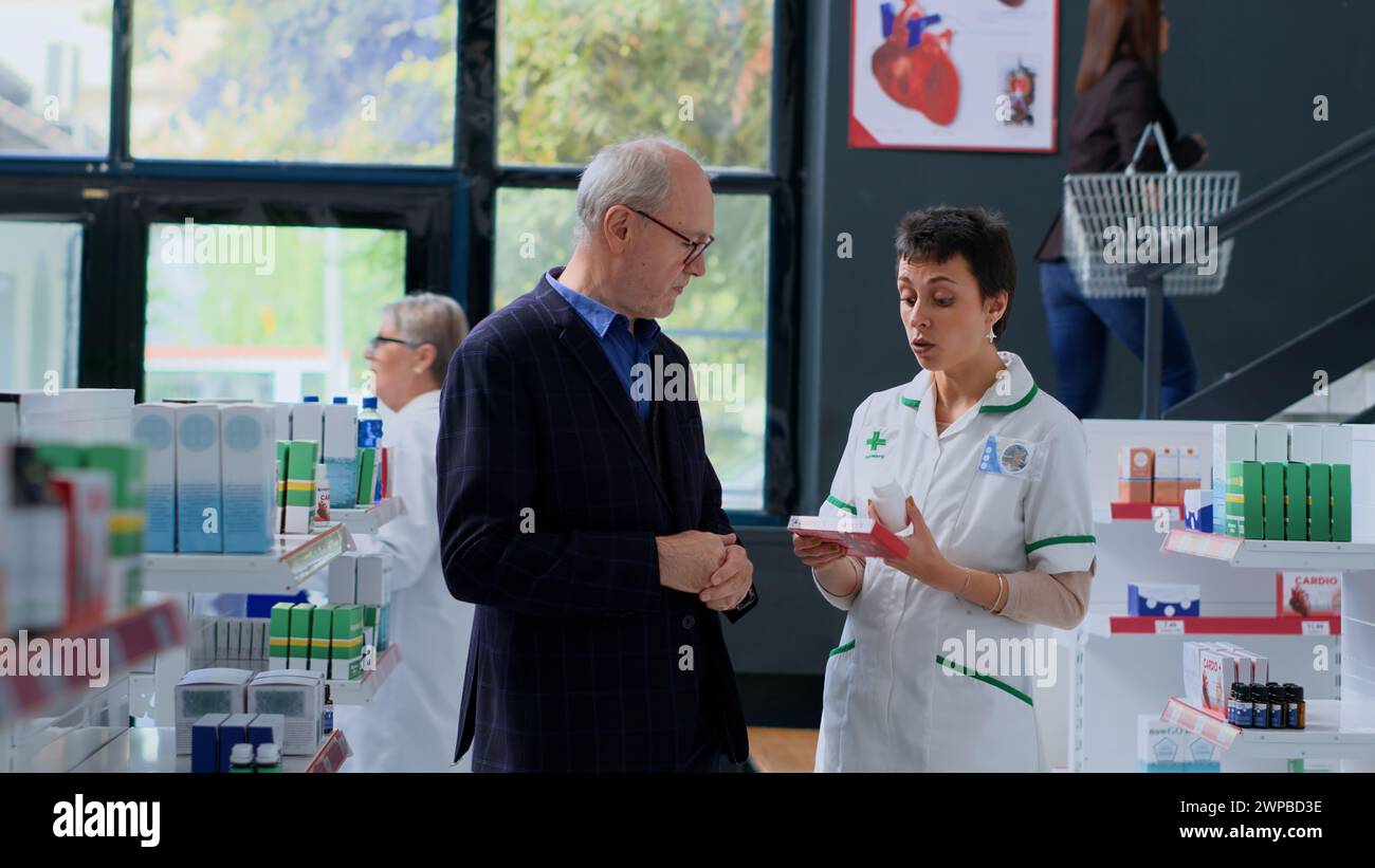 Pharmacien expérimenté en pharmacie offrant aux clients âgés des antibiotiques conçus pour traiter les symptômes de la maladie. Expert en soins de santé dans un magasin de pharmacie aidant l'homme âgé à se débarrasser des maux de cœur Banque D'Images