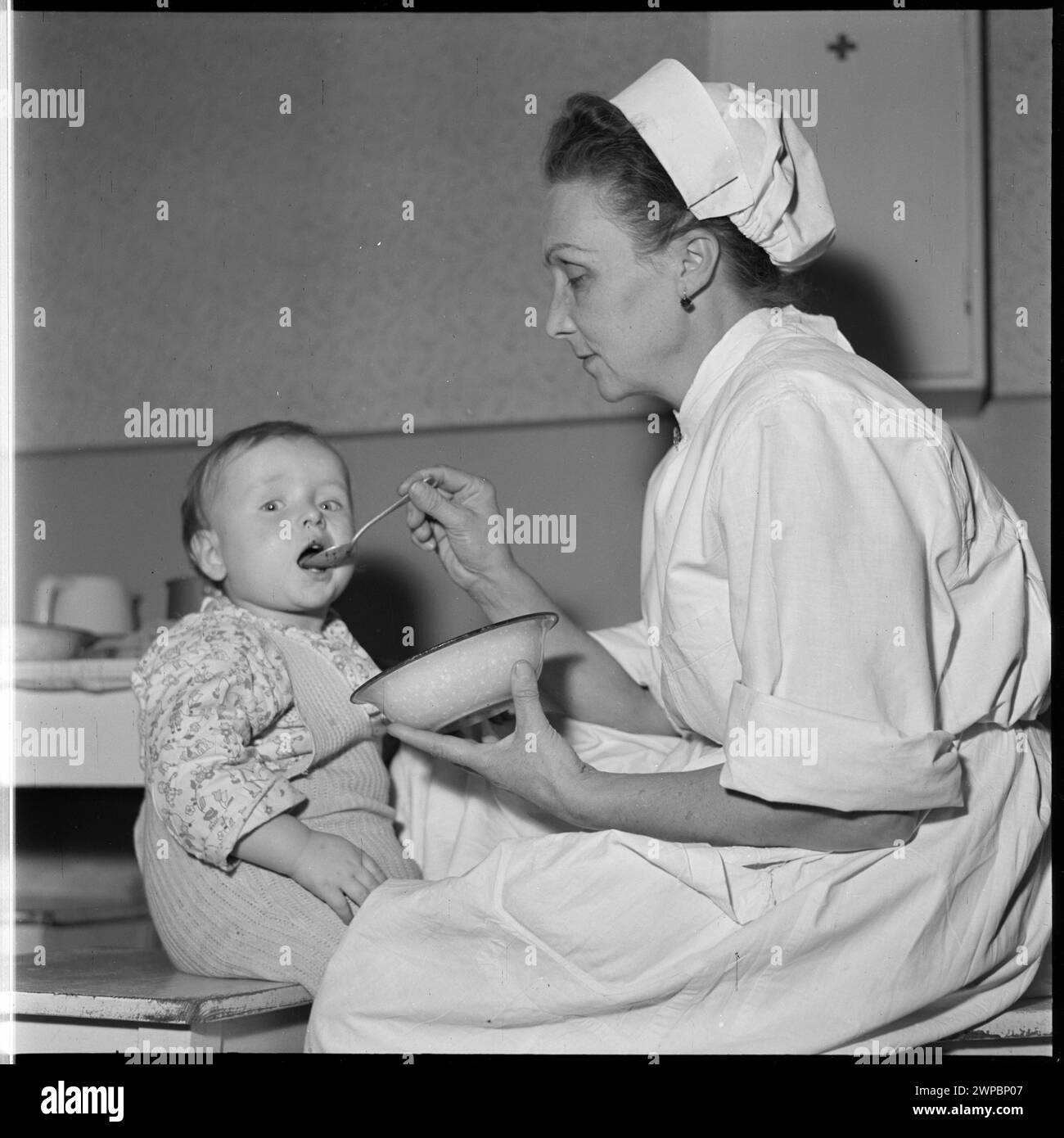 Photographie d'une baby-sitter nourrissant un enfant dans la pépinière de l'usine de l'industrie du coton de l'État à Pabianice. Fait partie de la série de photos de Wiesław Prażuch de 1953 à 1954 pour 'Fortuna Kruschów'. Banque D'Images