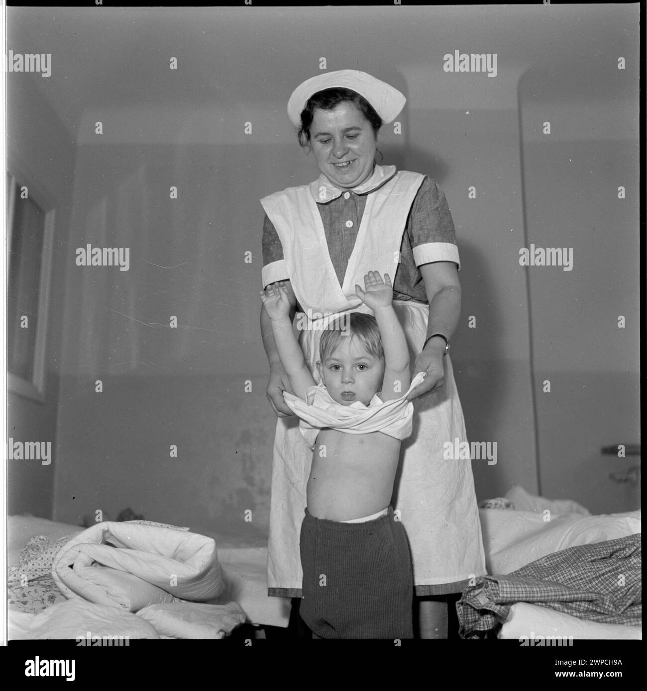 Photographie montrant une baby-sitter qui s'occupe d'un enfant dans une pièce de l'Obek et de la maternelle de l'usine industrielle de Pabianice, faisant partie d'une série de 1953. Banque D'Images