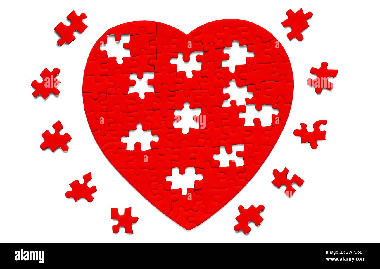 Gros plan d'un puzzle rouge en forme de cœur avec quelques éléments finaux à mettre en place disposés sur un fond blanc immaculé. Banque D'Images