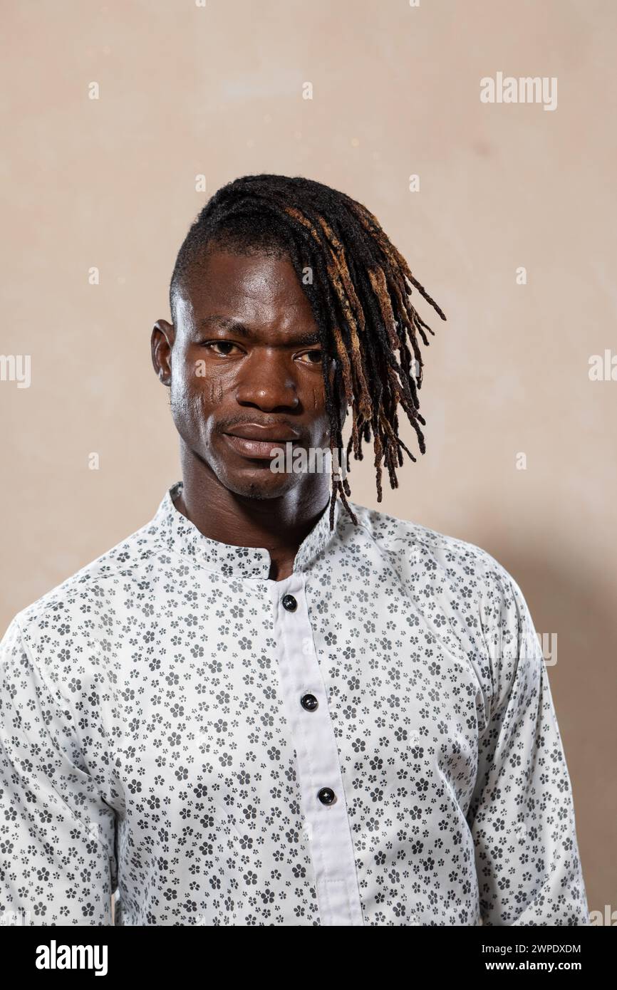 Jeune homme détendu avec des dreadlocks debout sur un fond neutre dans une chemise imprimée, reflétant le style moderne et la confiance décontractée Banque D'Images