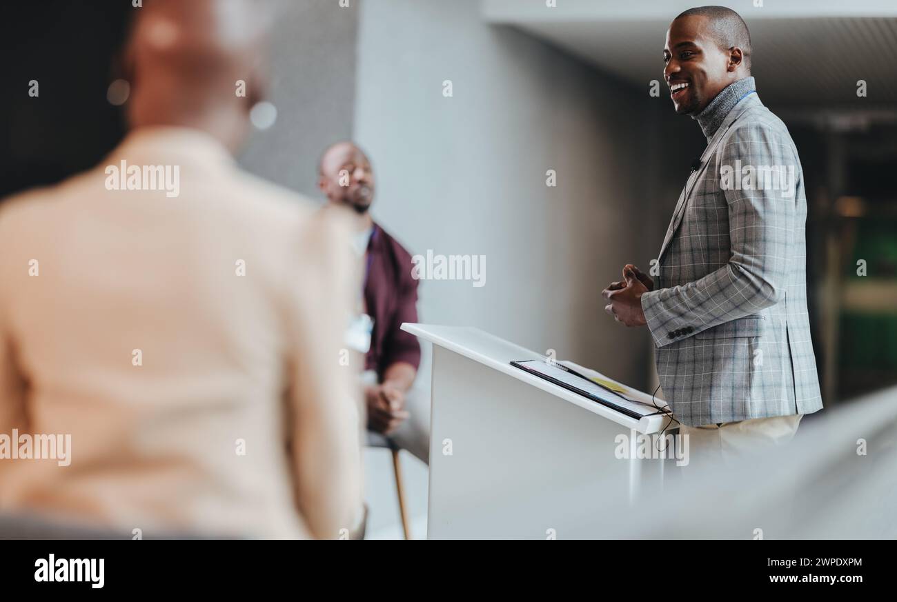 Homme d'affaires heureux se tient confiant tout en présentant à ses collègues dans un espace de bureau contemporain bien éclairé. Le focus sur le haut-parleur signifie leader Banque D'Images