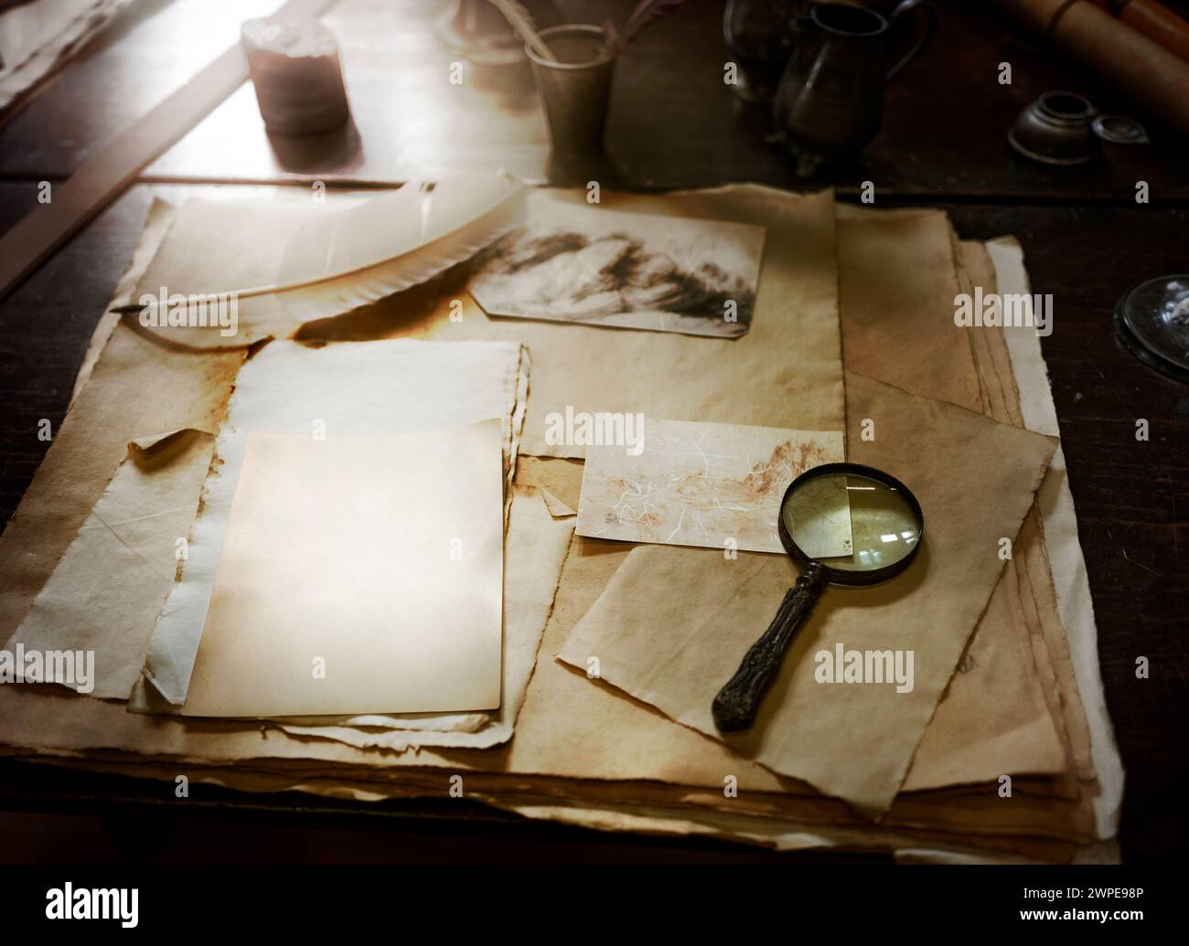 Mise au point peu profonde contre la table de travail médiévale dans une ambiance crépusculaire. Attrezzo avec plusieurs anciens papiers à dessin et ancienne loupe. Banque D'Images