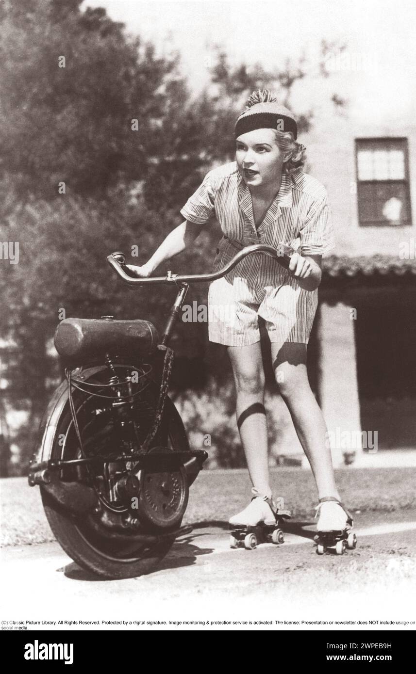 Dans les années 1930 Une femme sur des patins à roulettes tient sur le guidon d'une moto à une roue qui la tire vers l'avant. Elle a l'air concentrée quand la vitesse augmente. Banque D'Images