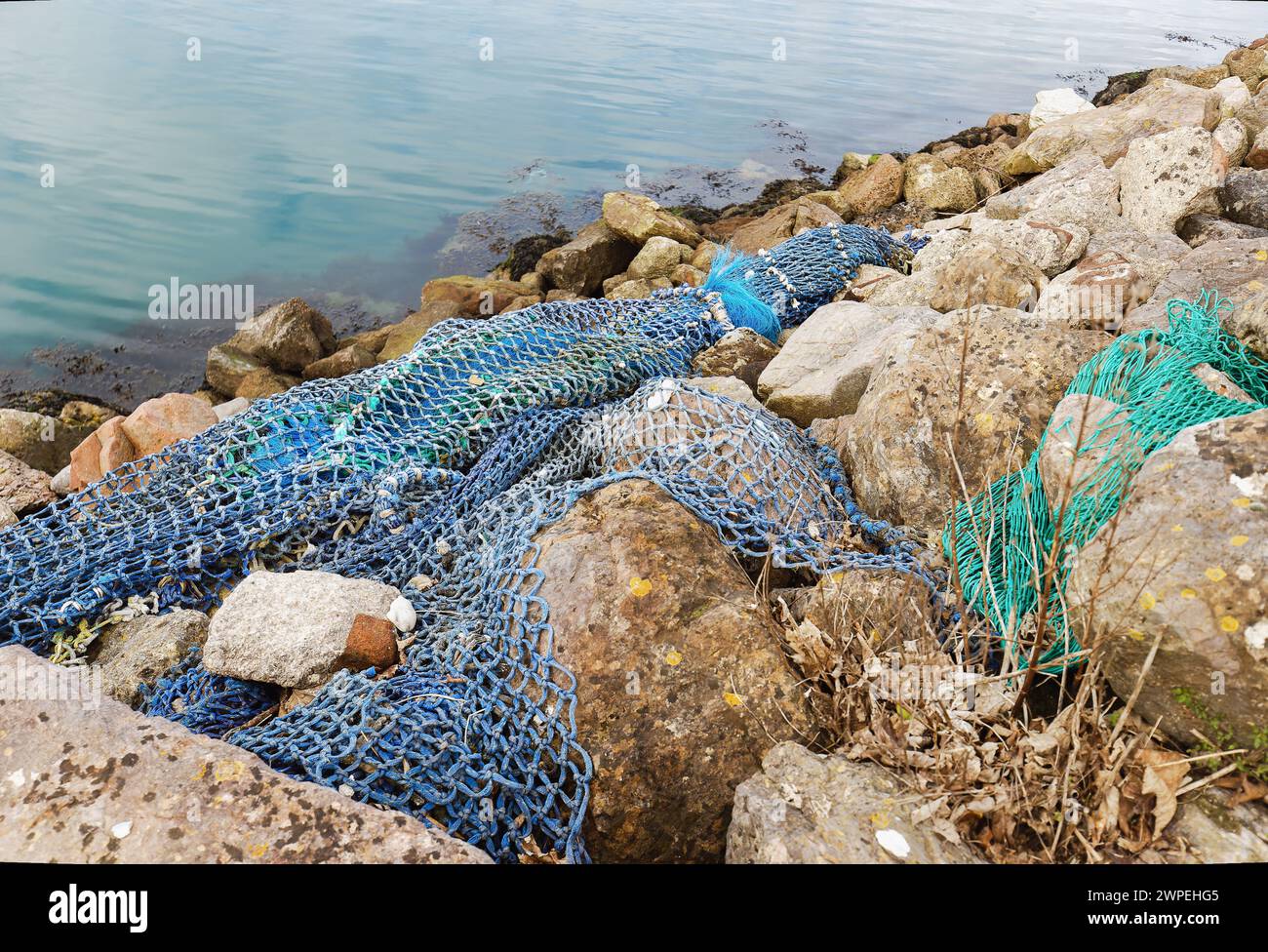 Image montrant des filets de pêche jetés échoués sur des rochers dans un port polluant l'environnement Banque D'Images