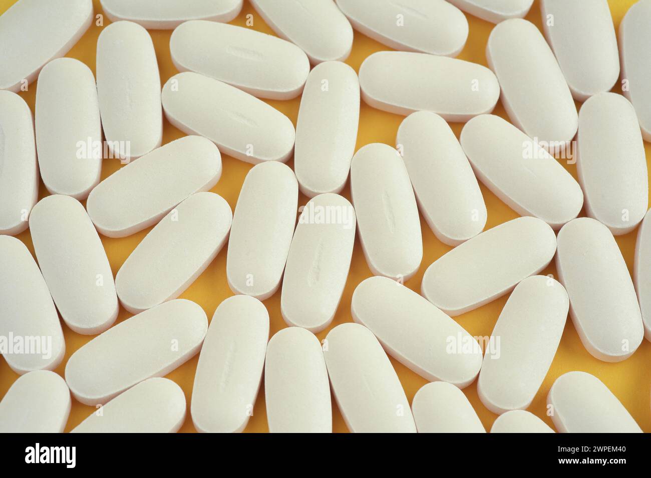 Photographie rapprochée vue du dessus d'un groupe de comprimés de vitamines blanches de forme ovale ou de pilules sur fond jaune. Vue de dessus. Banque D'Images