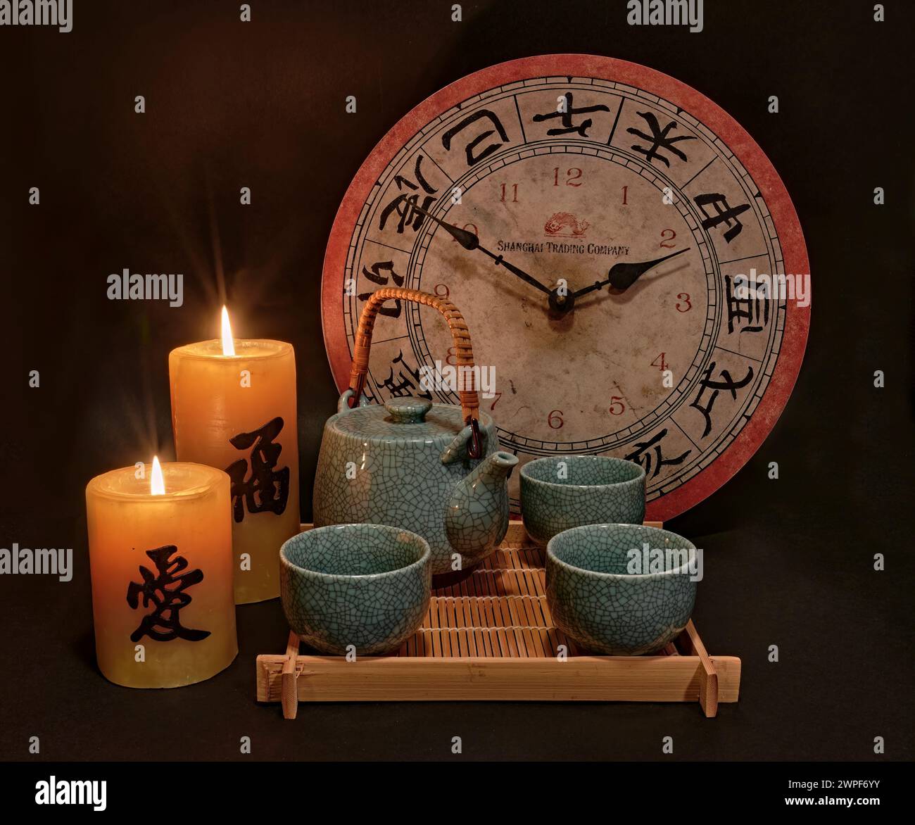 Une nature morte d'un service à thé avec une horloge. L'horloge a des chiffres asiatiques ou chinois. Avec deux bougies lisant santé et bonheur. Banque D'Images