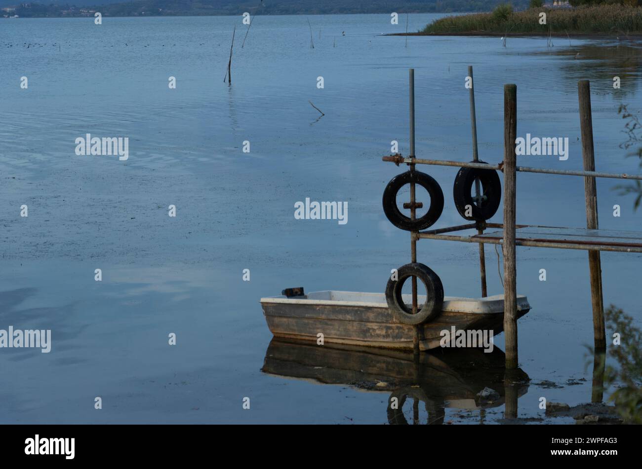 bateau amarré sur la rive d'un lac à côté d'une passerelle en fer et bois et pneus recyclés. Banque D'Images