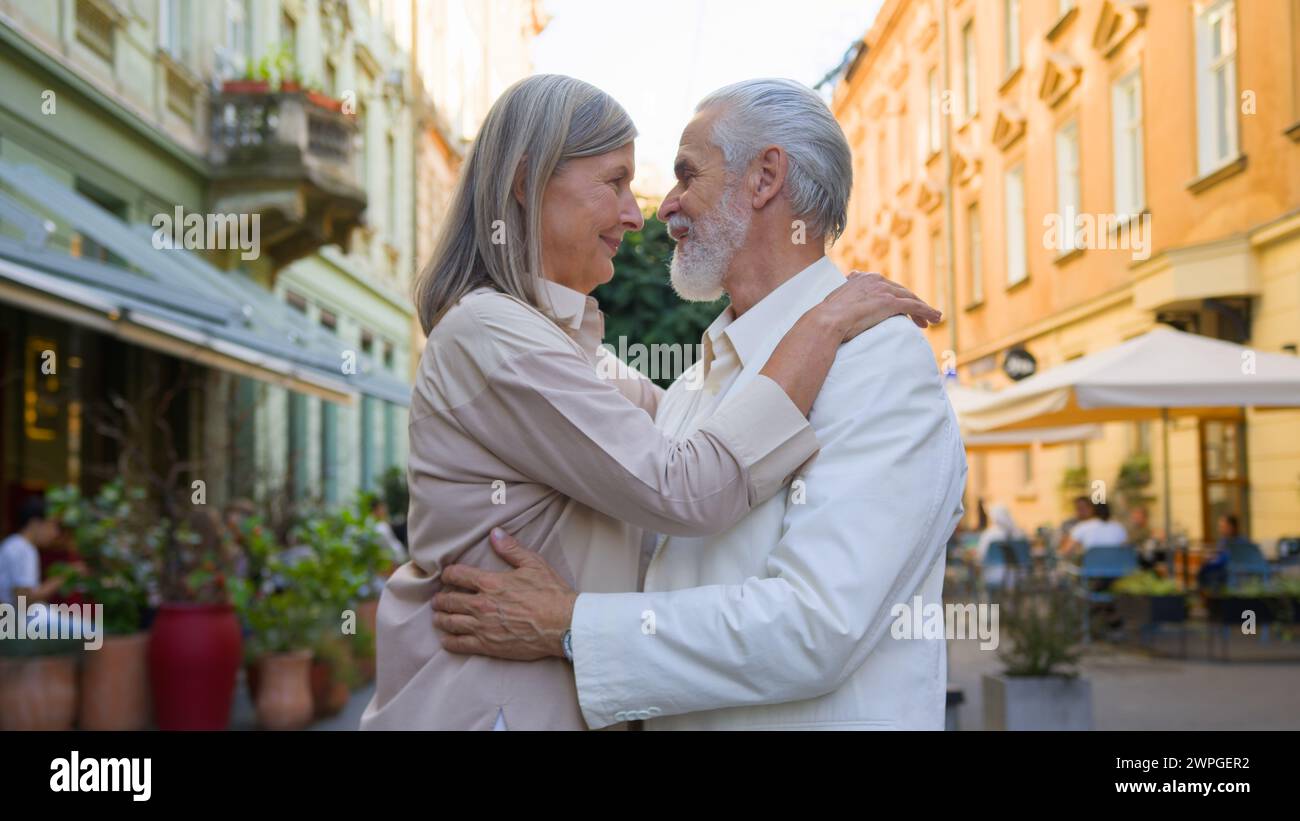 Dreamy senior Caucasien adulte mature gris-Hair couple femme homme regardant la caméra souriant embrassant câlin de liaison pensant bon avenir à l'extérieur. Médecine Banque D'Images
