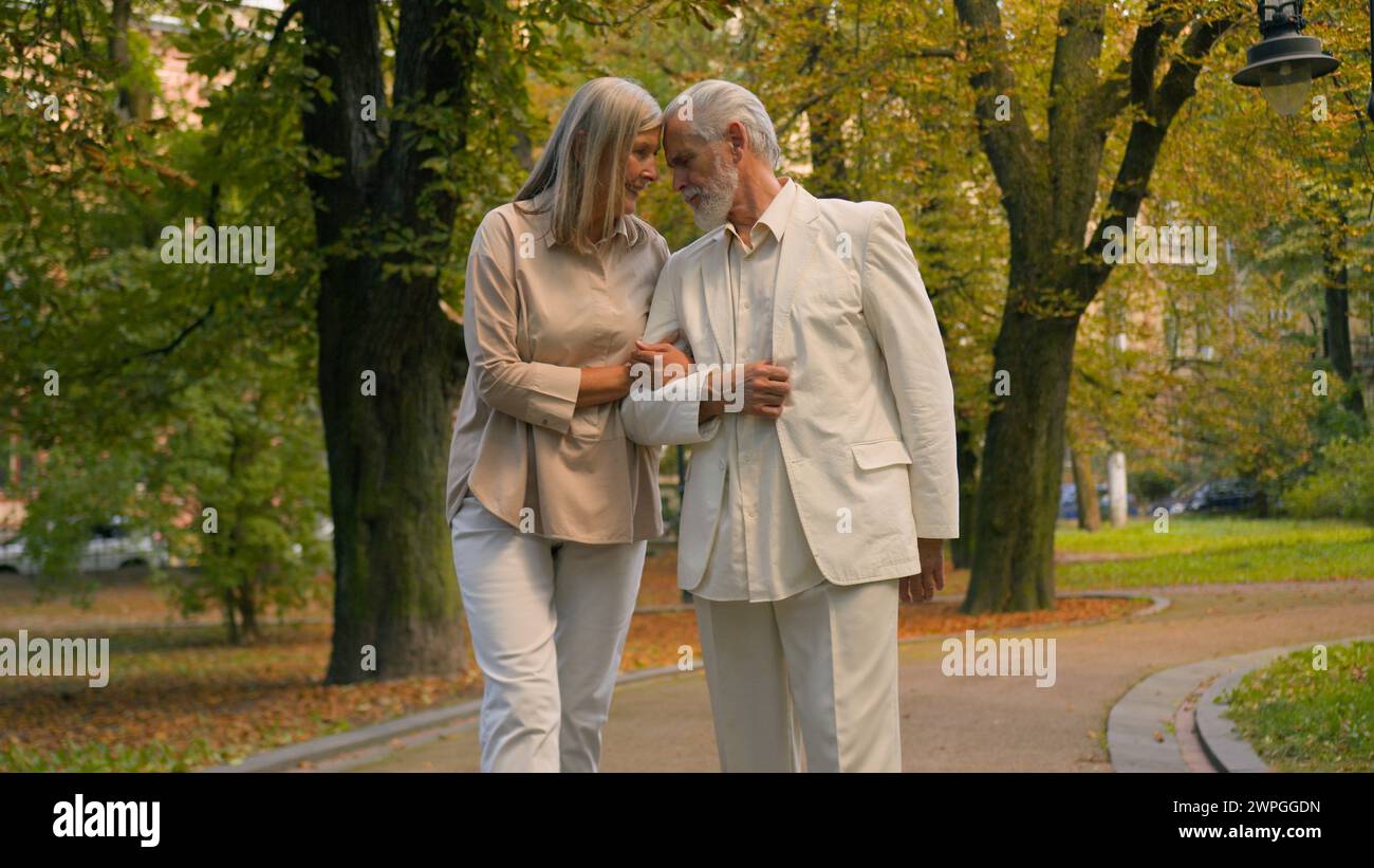 Heureux vieux en bonne santé aînés adultes caucasiens grands-parents mariés homme femme famille couple marchant la main à l'extérieur du parc de la ville racontant des histoires Banque D'Images