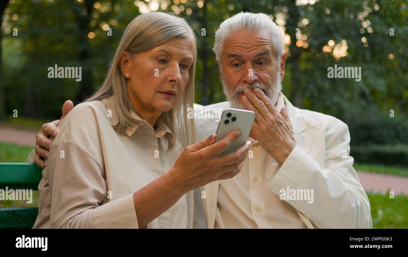 Inquiet âgé des années 70 famille caucasienne retraitée couple homme senior femme à l'aide de l'appareil de téléphone portable faisant défiler les utilisateurs de site Web Internet les clients parlant appel Banque D'Images