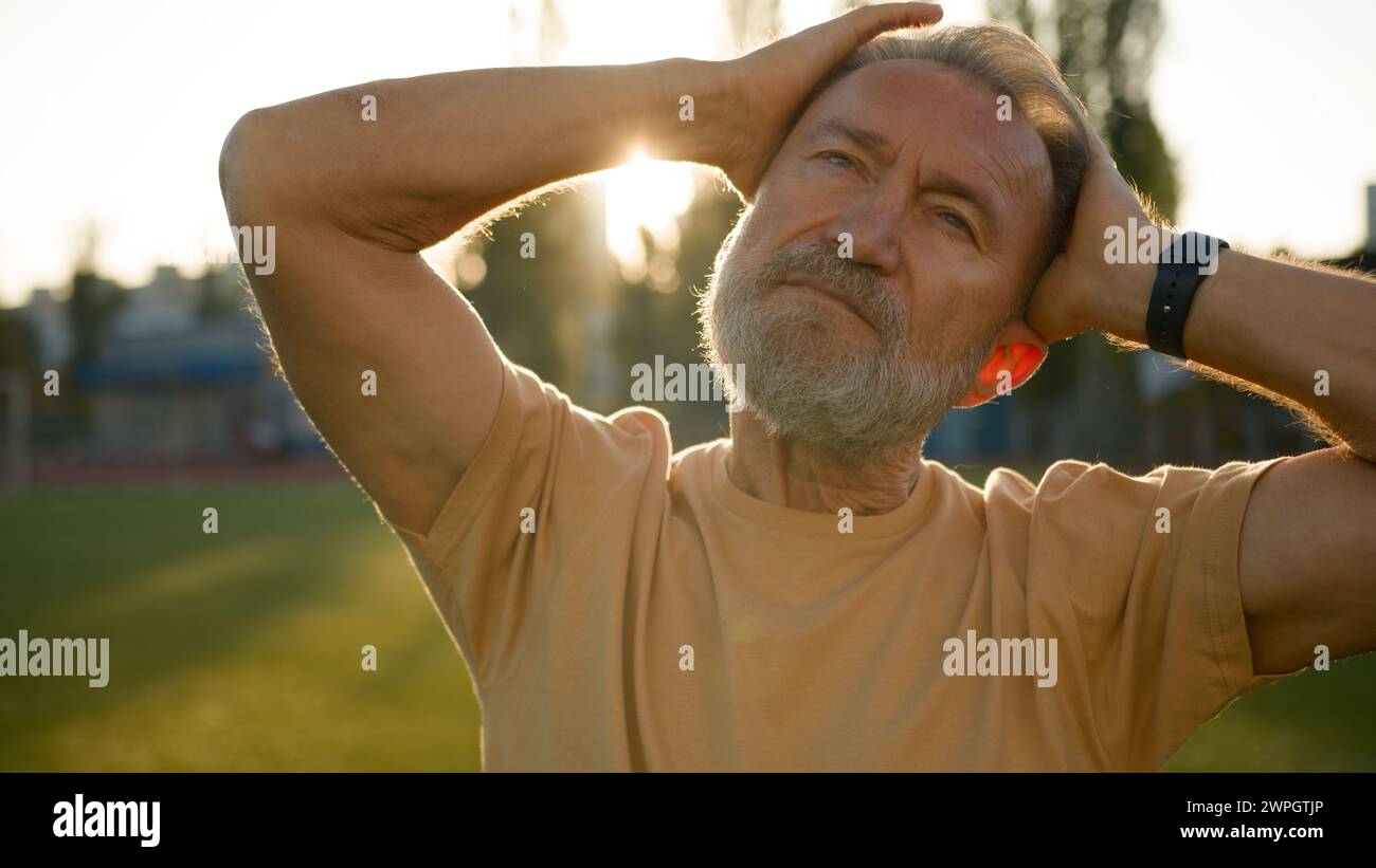 Gros plan caucasien européen retraité étirer muscles du cou tête sportif homme âgé échauffement flexibilité élastique Sunrise stade en plein air matin de la ville Banque D'Images
