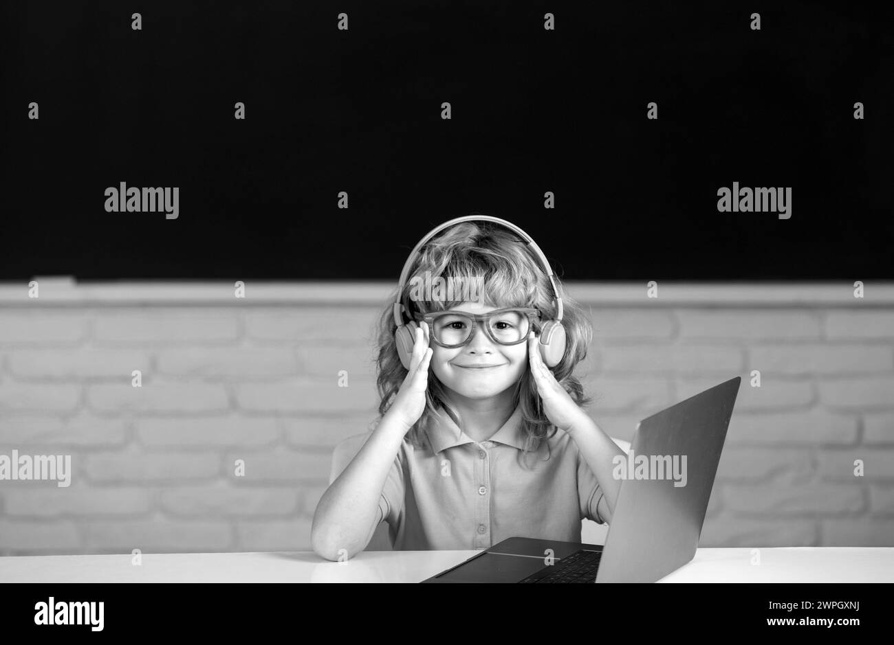 Smart boy dans un casque asseyez-vous au bureau, étudiez en ligne sur un ordinateur portable à l'école, klever Kid porter des écouteurs dans l'apprentissage d'ordinateur portable en utilisant des leçons d'Internet. Banque D'Images