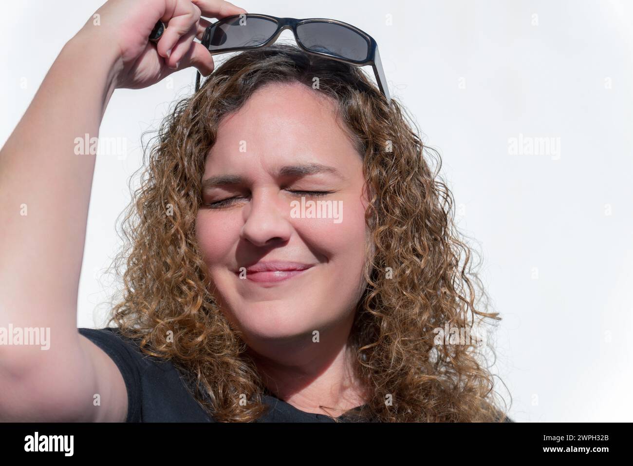 belle femme blonde aux cheveux bouclés agacée par le soleil avec ses yeux fermés met des lunettes de soleil Banque D'Images