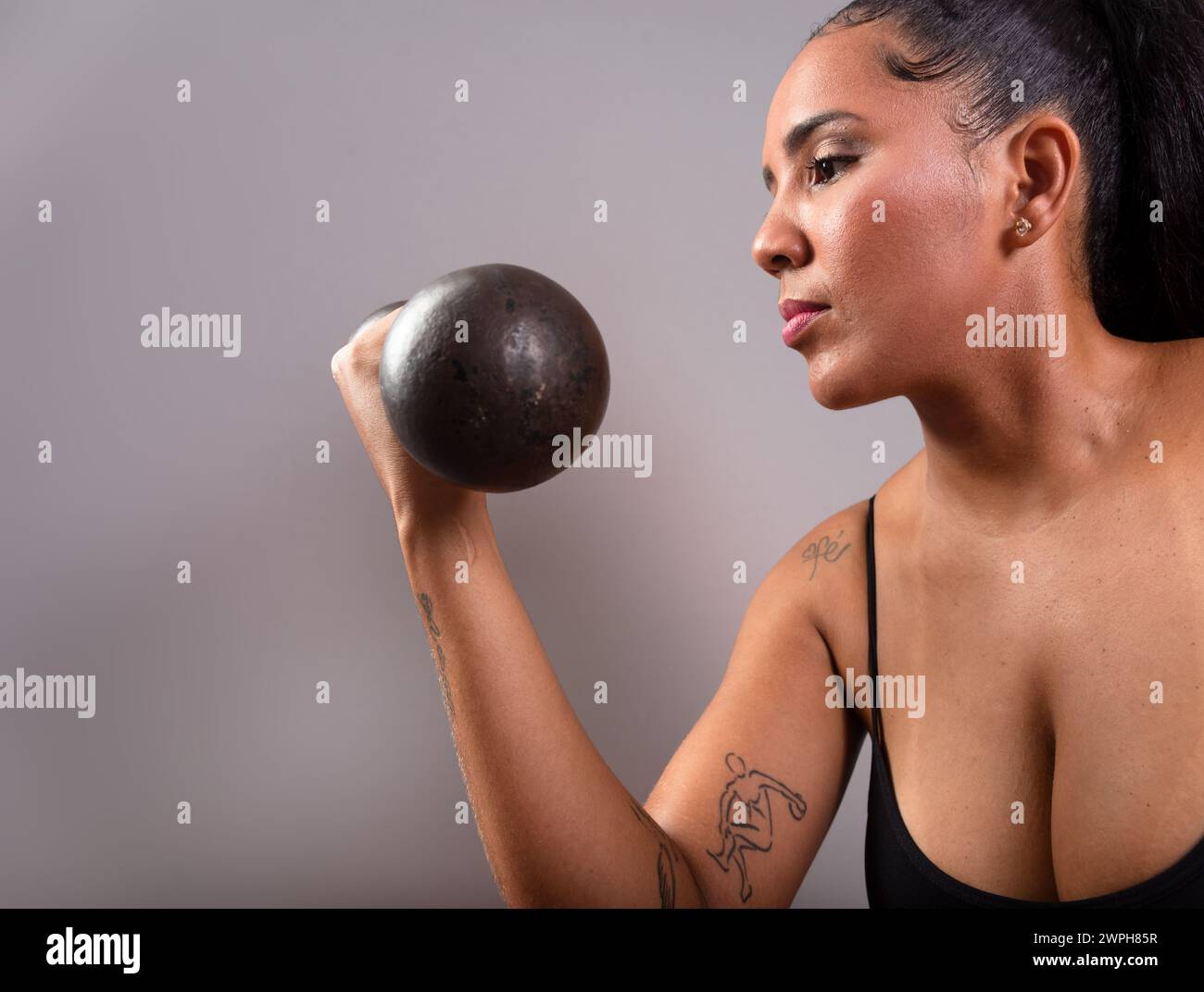 Belle femme brune, en vêtements de gym, assise faisant des exercices avec des haltères. Une vie saine. Sur fond gris. Banque D'Images