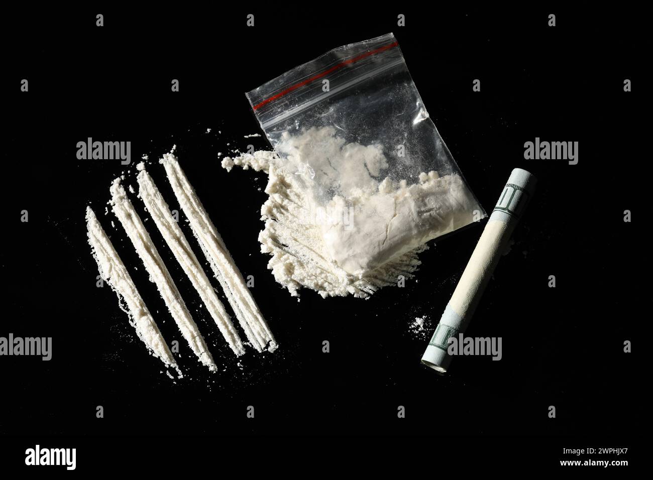 Toxicomanie. Sac en plastique avec cocaïne et billet de banque roulé dollar sur fond noir, plat Banque D'Images