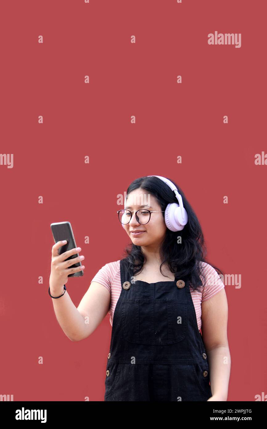 Une adolescente Latina de 17 ans utilise son téléphone portable et audio pour se connecter à de la musique, des livres audio podcast et des chansons avec ses amis Banque D'Images