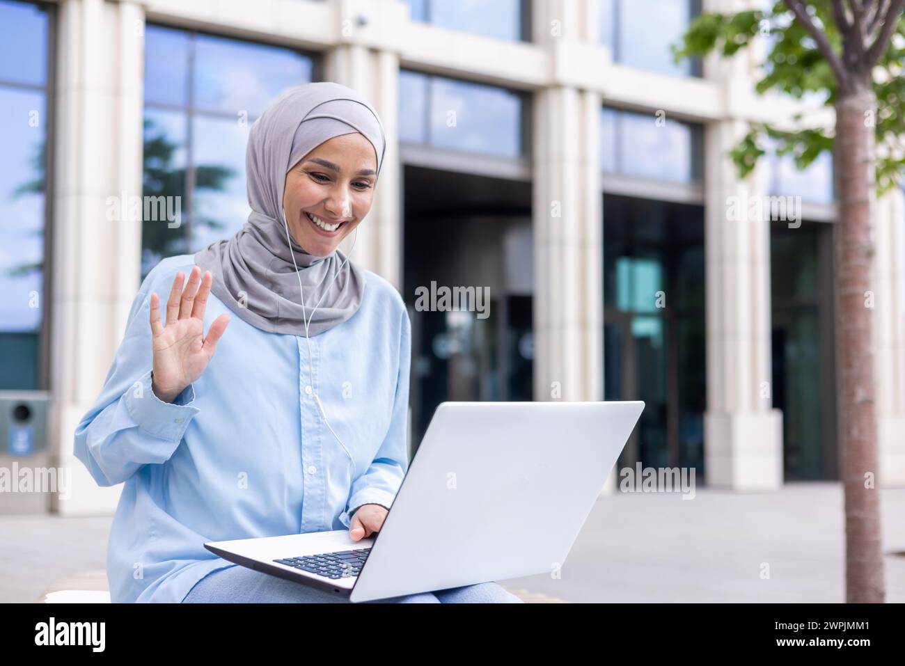 Joyeuse dame musulmane portant un hijab s'engageant dans un chat vidéo, agitant à la webcam avec un sourire joyeux à l'extérieur. Banque D'Images