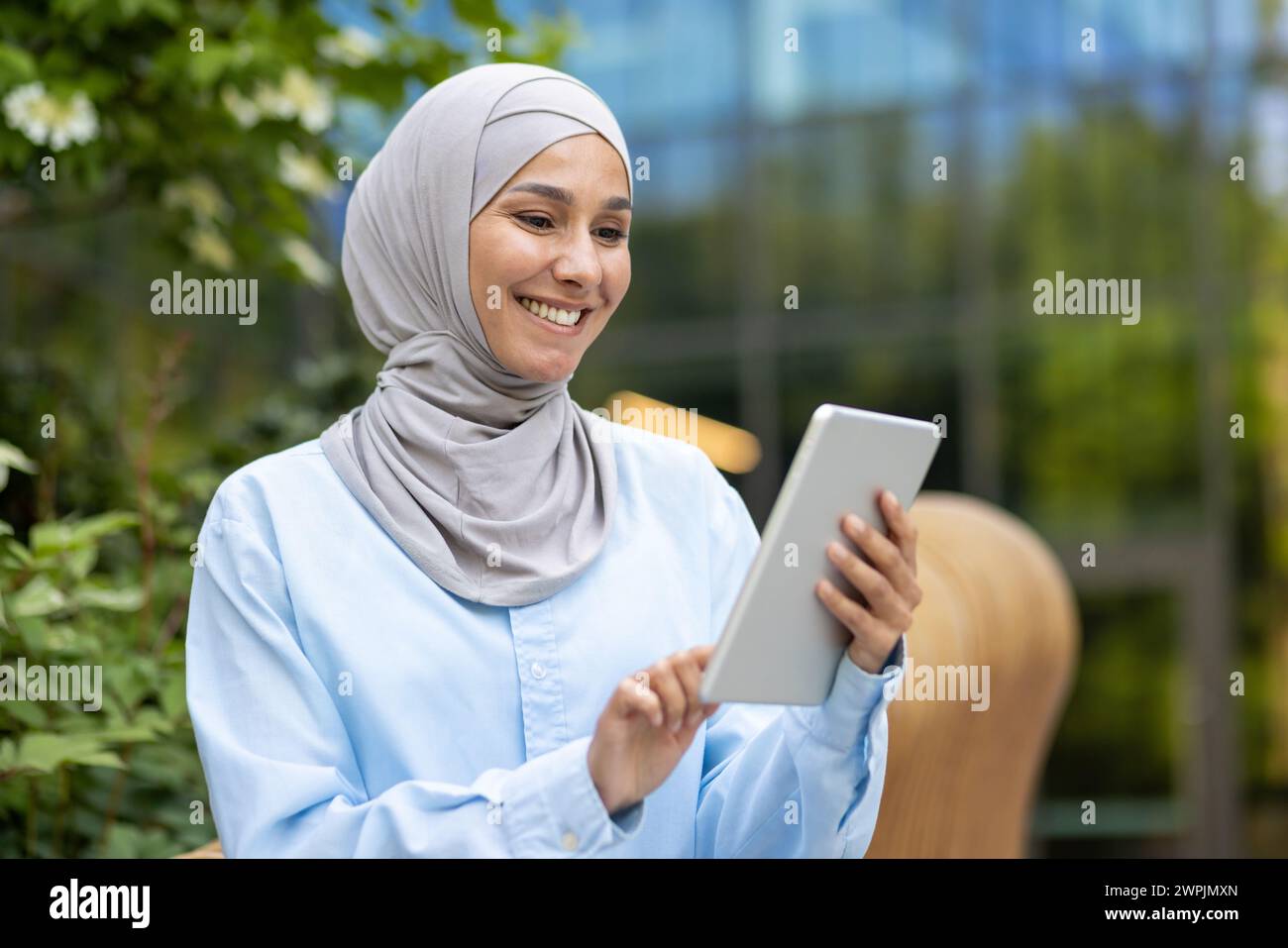 Femme musulmane heureuse professionnelle avec hijab tenant une tablette, profitant de la technologie en dehors d'un cadre de bureau moderne. Banque D'Images