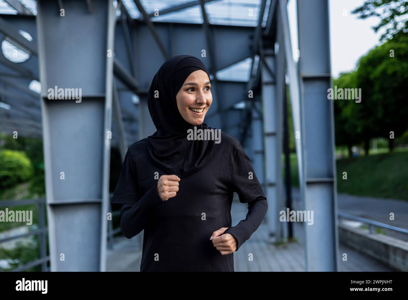 Une femme musulmane joyeuse portant un hijab aime courir dans un parc urbain, exsudant la santé et le bonheur. Banque D'Images