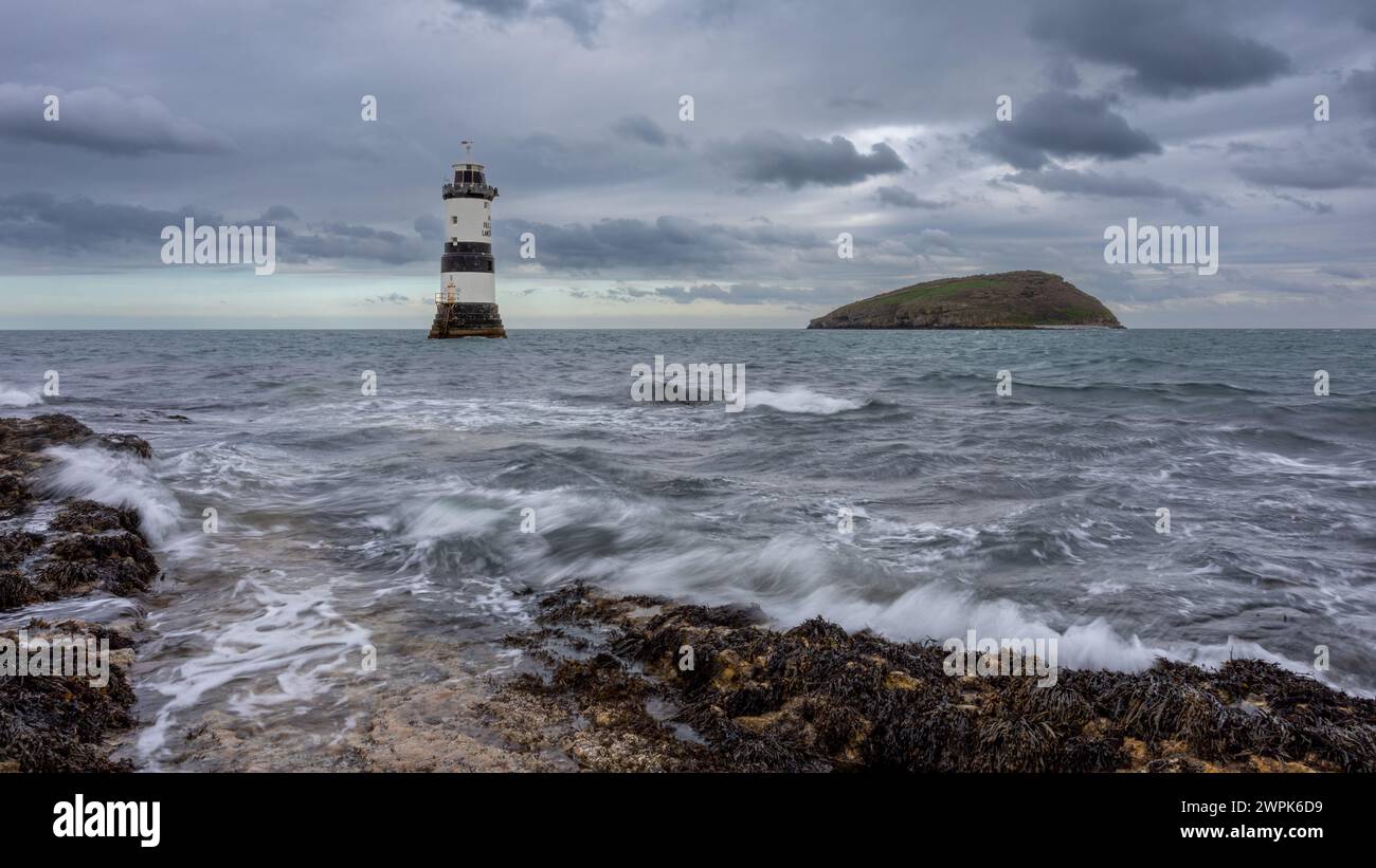 Un point de vue bas et une longue exposition pour montrer le mouvement dans les vagues. Pen mon point au phare de Trwyn du et au loin est l'île des macareux Banque D'Images