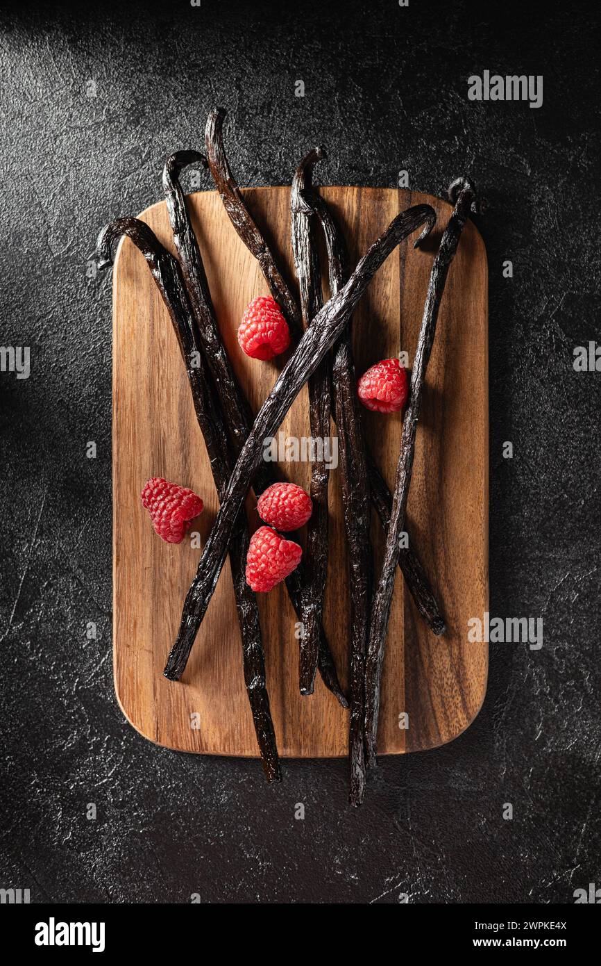 Haricots de vanille avec des framboises sur une planche de bois Banque D'Images