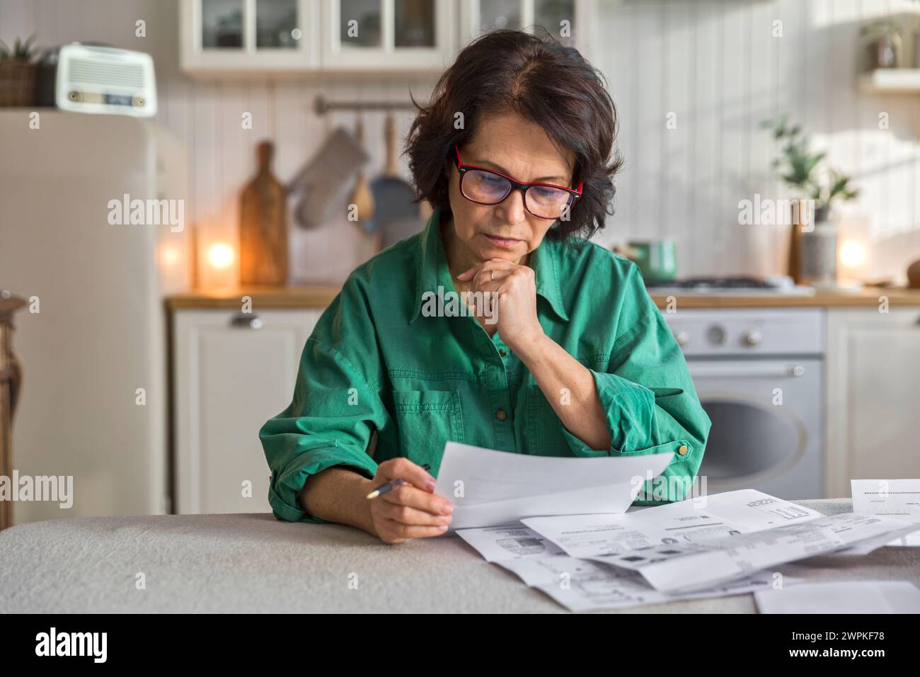 femme âgée examine les papiers et les factures, assis dans la cuisine Banque D'Images