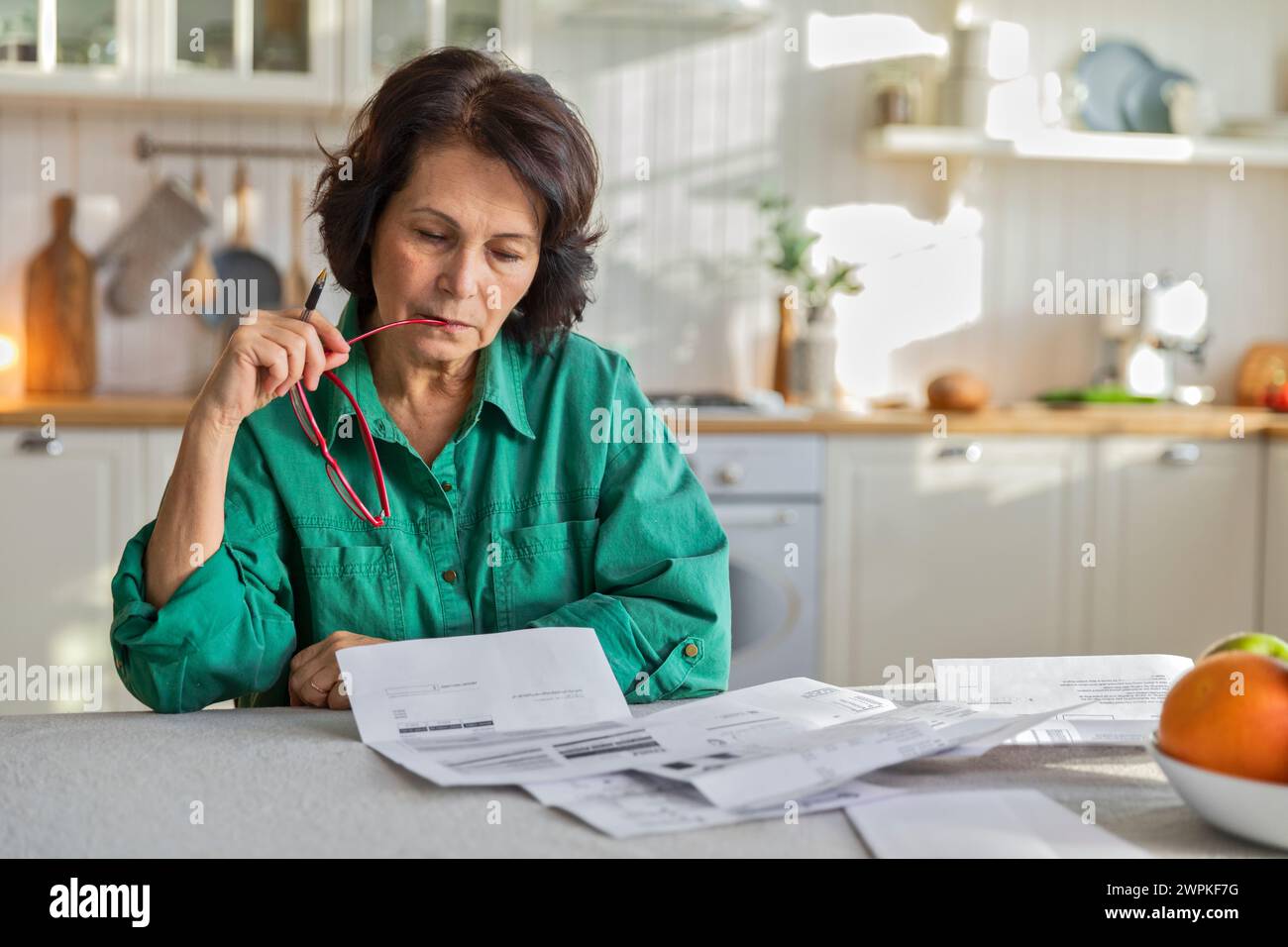 une femme âgée réfléchie examine les papiers et les factures, assise dans la cuisine Banque D'Images