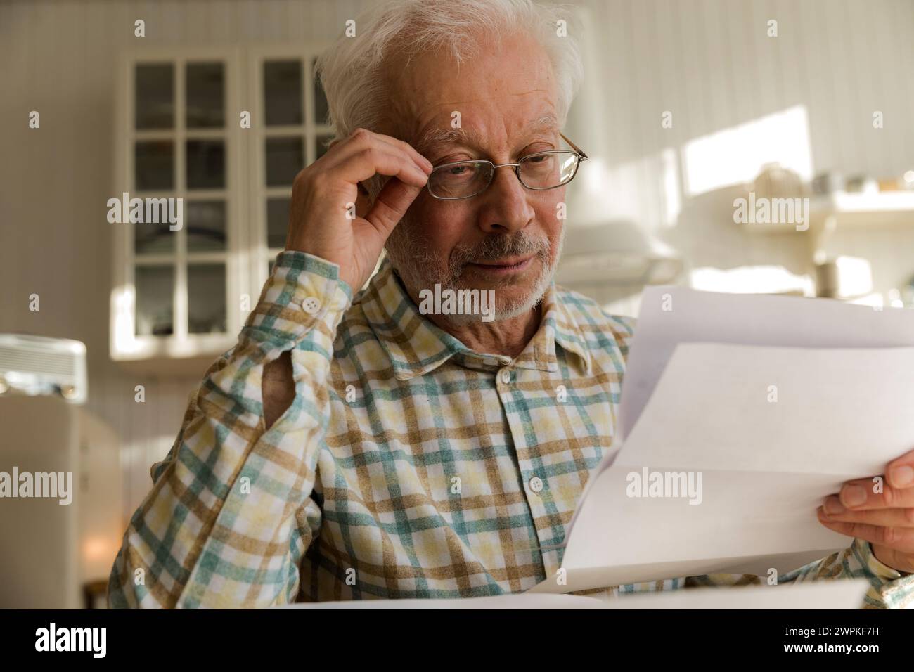 homme âgé assis avec des factures et des taxes dans la cuisine, lecture Banque D'Images