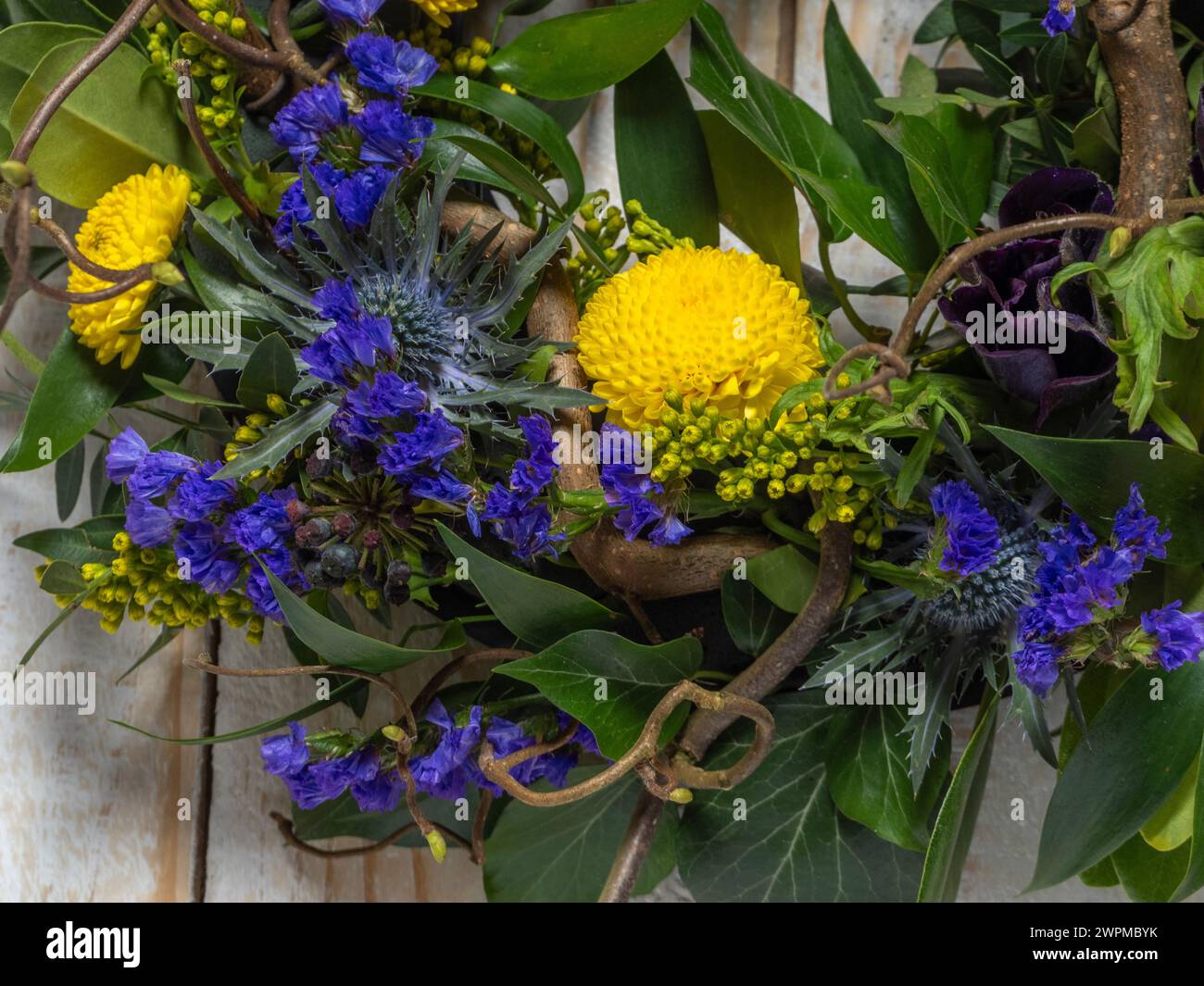Gros plan d'une couronne printanière avec des fleurs violettes et jaunes et des brindilles torsadées de noisette, sur un fond rustique en bois blanchi à la chaux. Banque D'Images