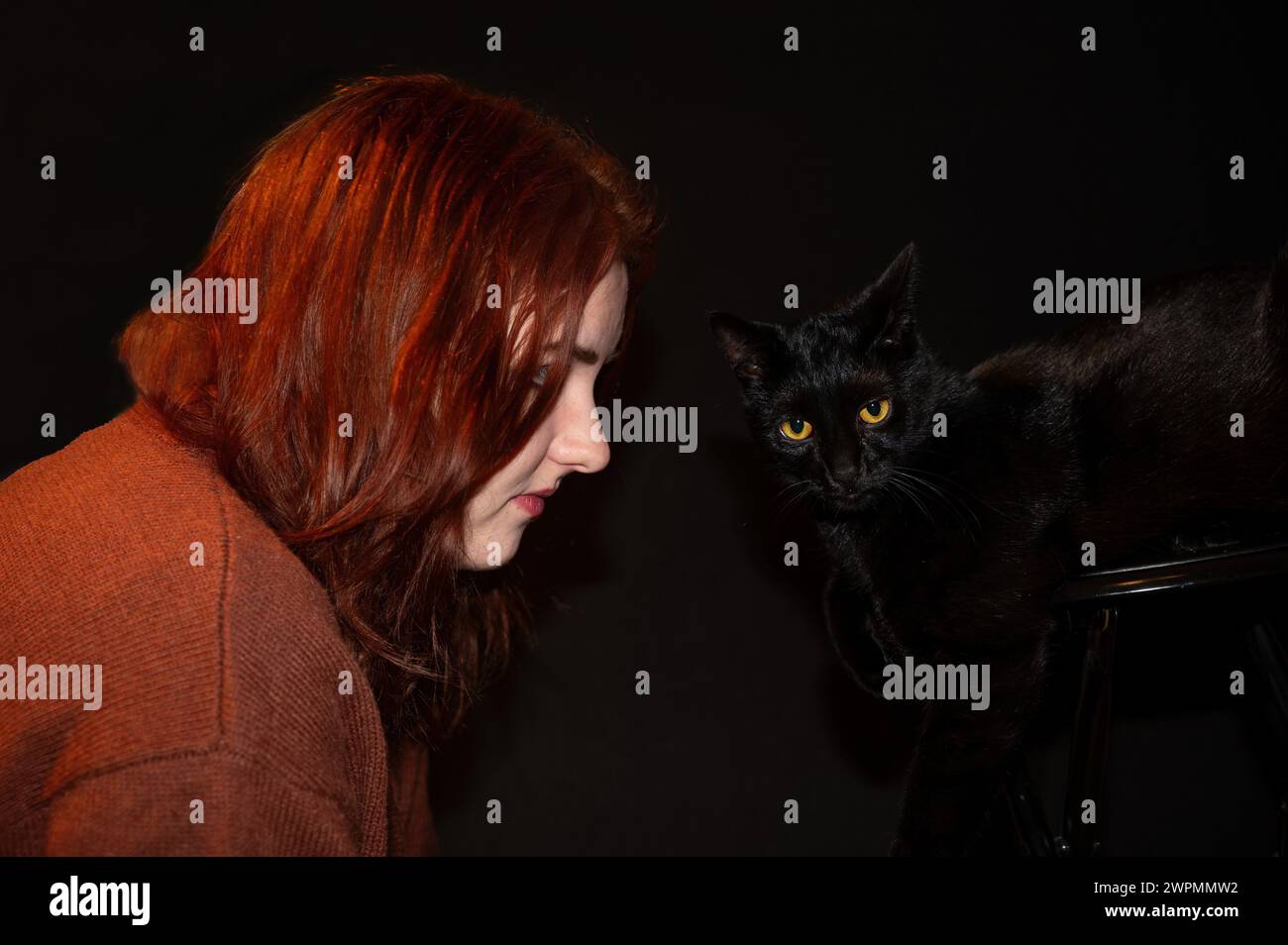 Une fille aux cheveux roux avec son chat noir et son fond noir Banque D'Images