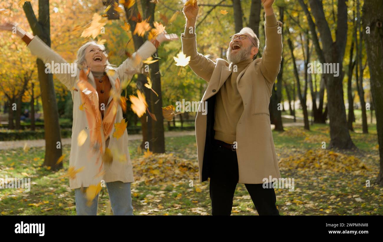 Heureux insouciant vieux couple caucasien amour femme retraitée et homme jetant des feuilles jaunes dans la forêt de parc d'automne ensemble profiter de feuilles tombées drôle mature Banque D'Images
