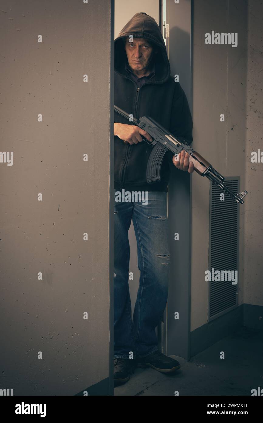 Homme en chemise à capuche noire armé d'un pistolet automatique à la recherche d'un danger Banque D'Images