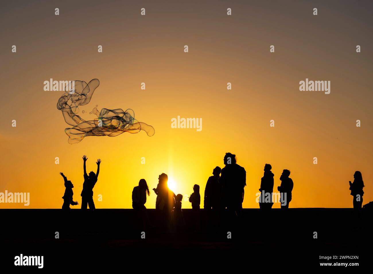 Enfants jouant avec de grandes bulles sur la promenade au coucher du soleil, Meloneras, Gran Canaria, Espagne, Europe Banque D'Images