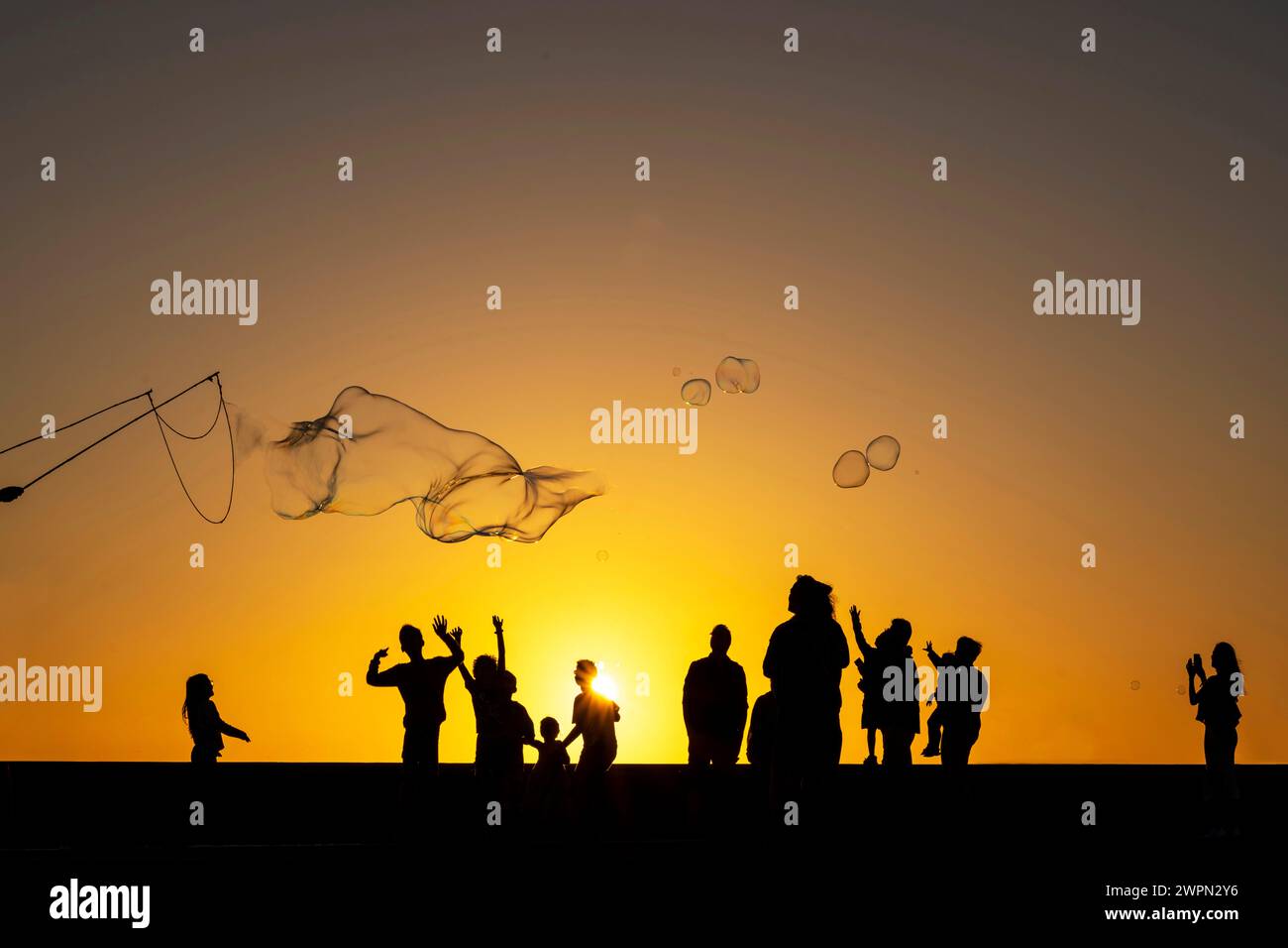 Enfants jouant avec de grandes bulles sur la promenade au coucher du soleil, Meloneras, Gran Canaria, Espagne, Europe Banque D'Images