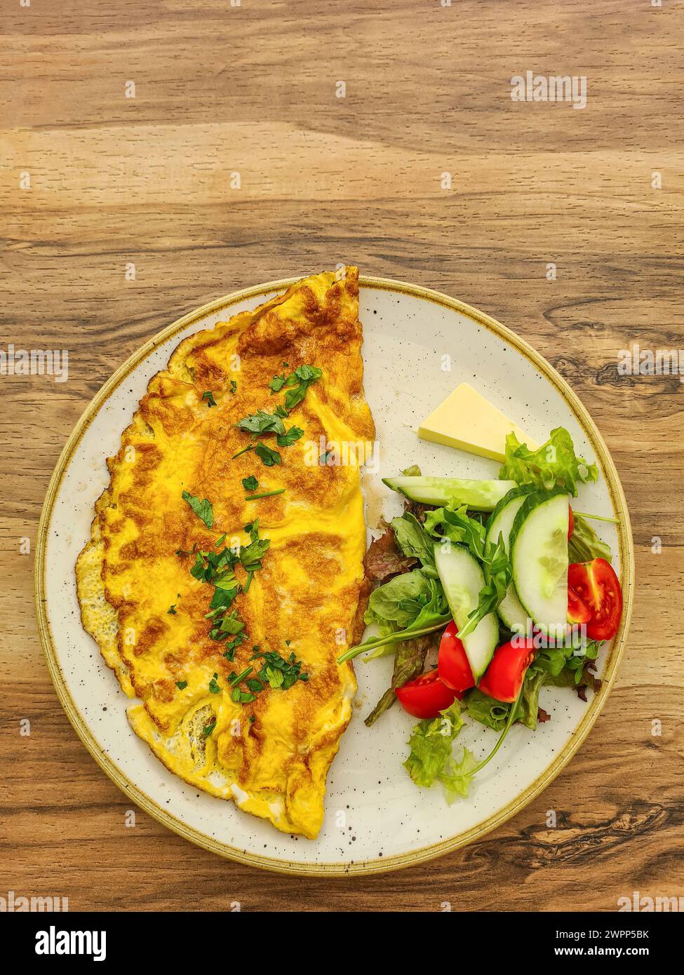 Copieux omelette au persil servi dans une assiette avec concombre, tomates tranchées, salade, beurre, omelette Banque D'Images